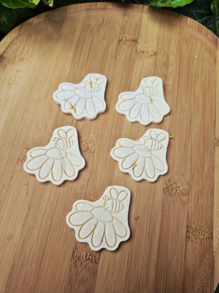Vijf Wunderblooms hondenkoekjes in bloemvorm met een gegraveerd bijtje op een houten serveerplank. Ambachtelijk gebakken hondensnacks van Wunderbark Pawstry.