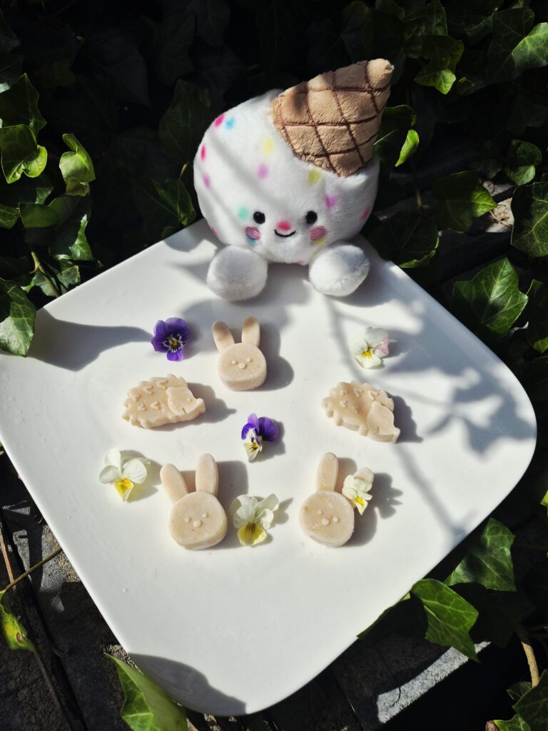 Gelato Scoops Gojibes hondenijsjes op basis van geitenmelk in schattige konijnen- en egelvormen, gemaakt met natuurlijke gojibes en gepresenteerd op een wit bord met eetbare viooltjes. Onderschrift