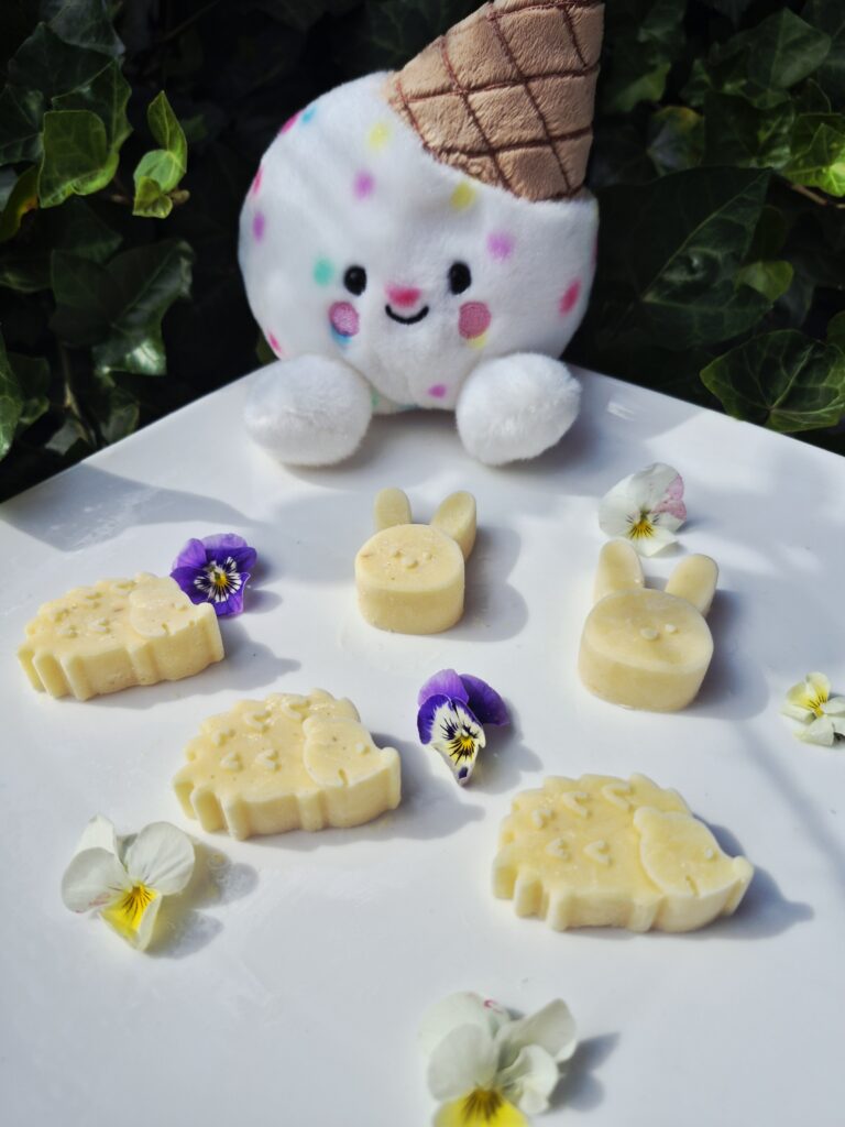 Gelato Scoops Ananas hondenijsjes op basis van geitenmelk in vrolijke ijsvormen, gemaakt met natuurlijke ananas en gepresenteerd op een wit bord met eetbare viooltjes.