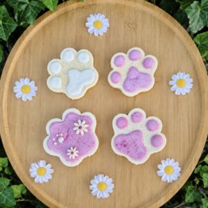 Poezelpootje hondenkoekje met roze icing, versierd met witte bloemetjes en een klein pootafdrukje.